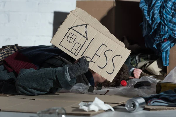 Obdachloser Liegt Auf Müll Mit Haussymbol Und Weniger Schriftzug Auf — Stockfoto