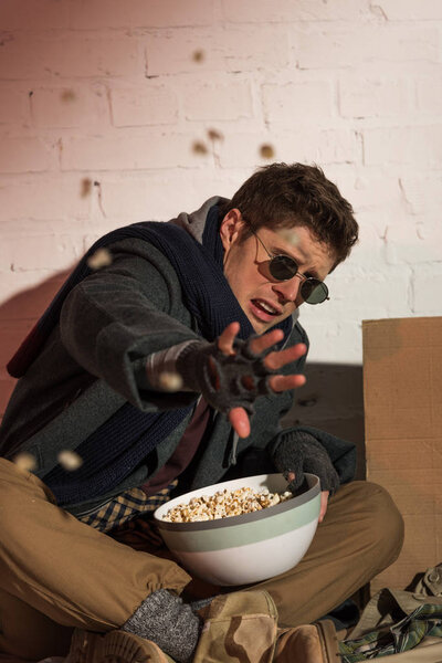 angry homeless man throwing pop corn from bowl at camera
