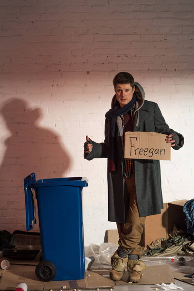 homeless man showing ok sign and holding cardboard card with "freegan" inscription