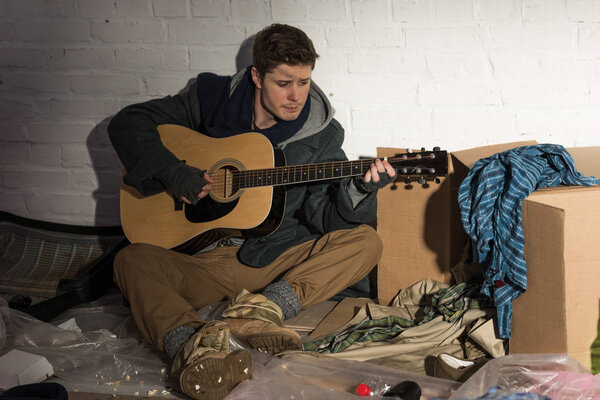 homeless man playing guitar while sitting on rubbish dump
