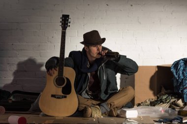 gitar tutarak ve sokak çöp dökümü üzerinde otururken alkol Şişeden içme evsiz adam