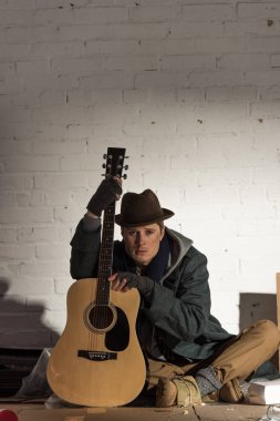 üzgün evsiz adam tuğla duvar dibinde oturan gitar ile