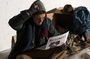 etkilenen evsiz adamın çöp tarafından çevrili otururken iş gazete okuma
