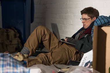 evsiz adam çöp dökümü üzerinde otururken dizüstü bilgisayar kullanarak