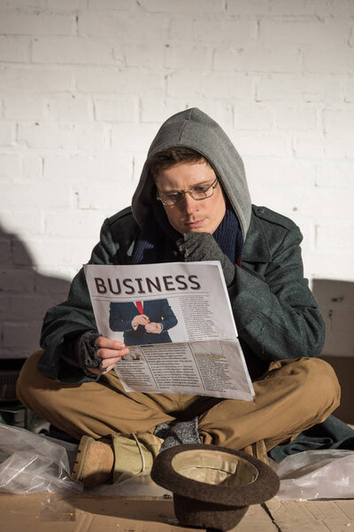 homeless man in glasses attentively reading business newspaper 
