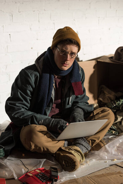 serious homeless man in glasses using laptop