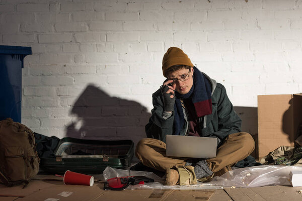 homeless man using laptop while sitting surrounded by rubbish