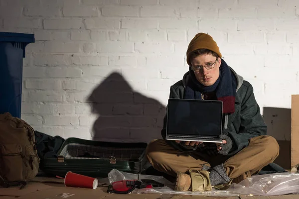 レンガの壁はゴミ捨て場のそばに座ってラップトップを使用して深刻なホームレスの男性 — ストック写真