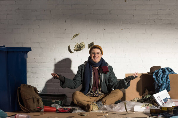 smiling homeless man tossing money while on garbage dump