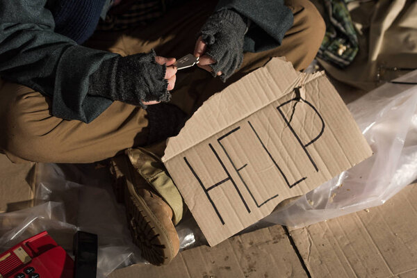 cropped view of homeless man sitting with cardboard card with "help" handwritten text