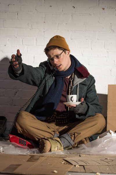 homeless man holding coffee cup and using vintage phone