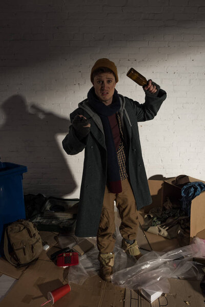 пьяный бездомный держит пустую бутылку, стоя в угрожающей позе
