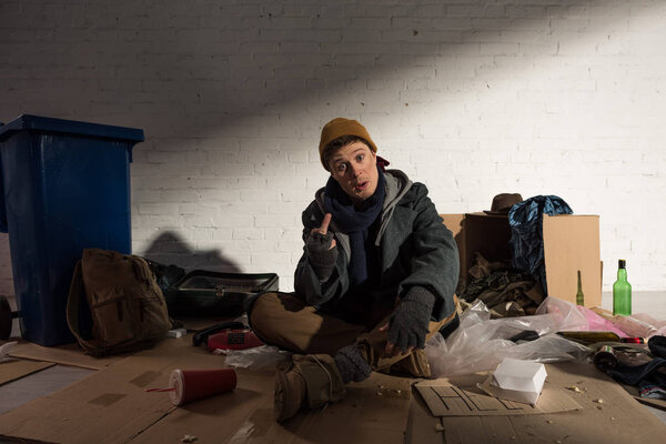 homeless man showing middle finger while sitting on rubbish dump