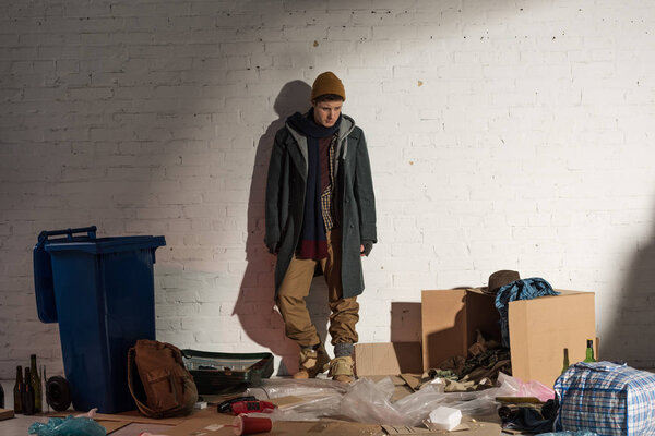 homeless man standing by white brick wall on rubbish dump
