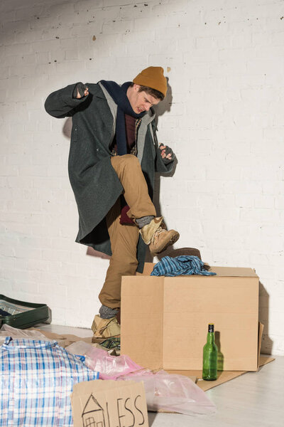 homeless man aggressively pushing rubbish into box by kicking