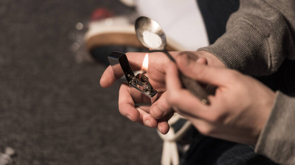 selective focus of junkie man boiling heroin in spoon on lighter