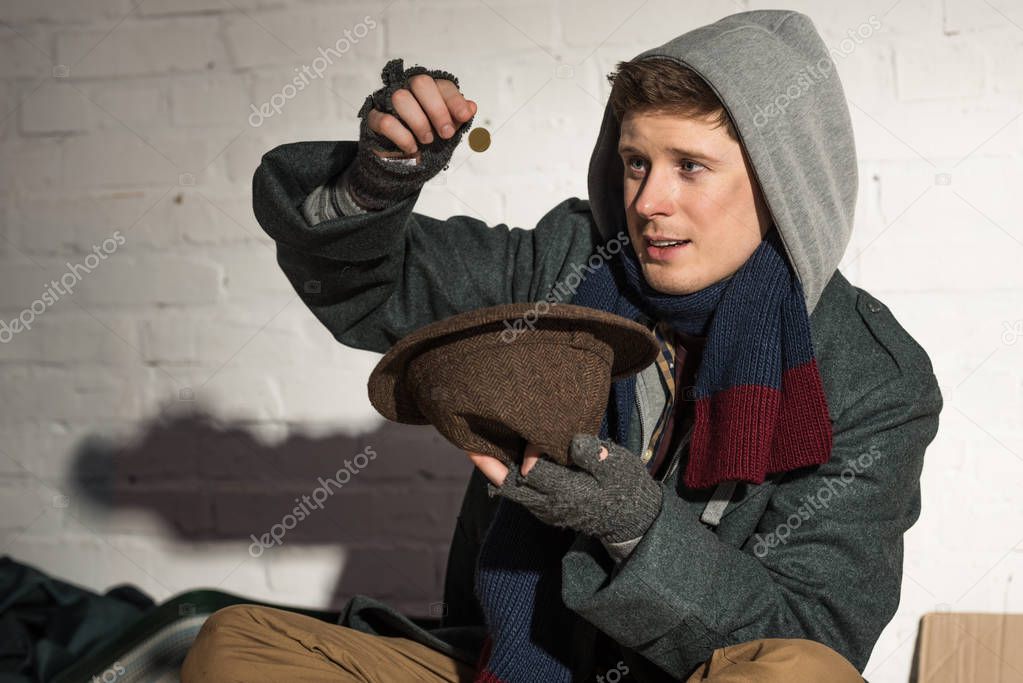 homeless man in hood throwing coin into hat