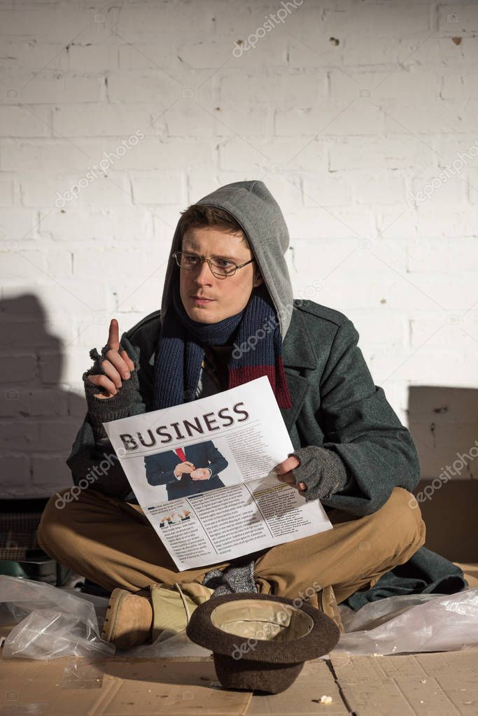 homeless man reading business newspaper and showing idea sign