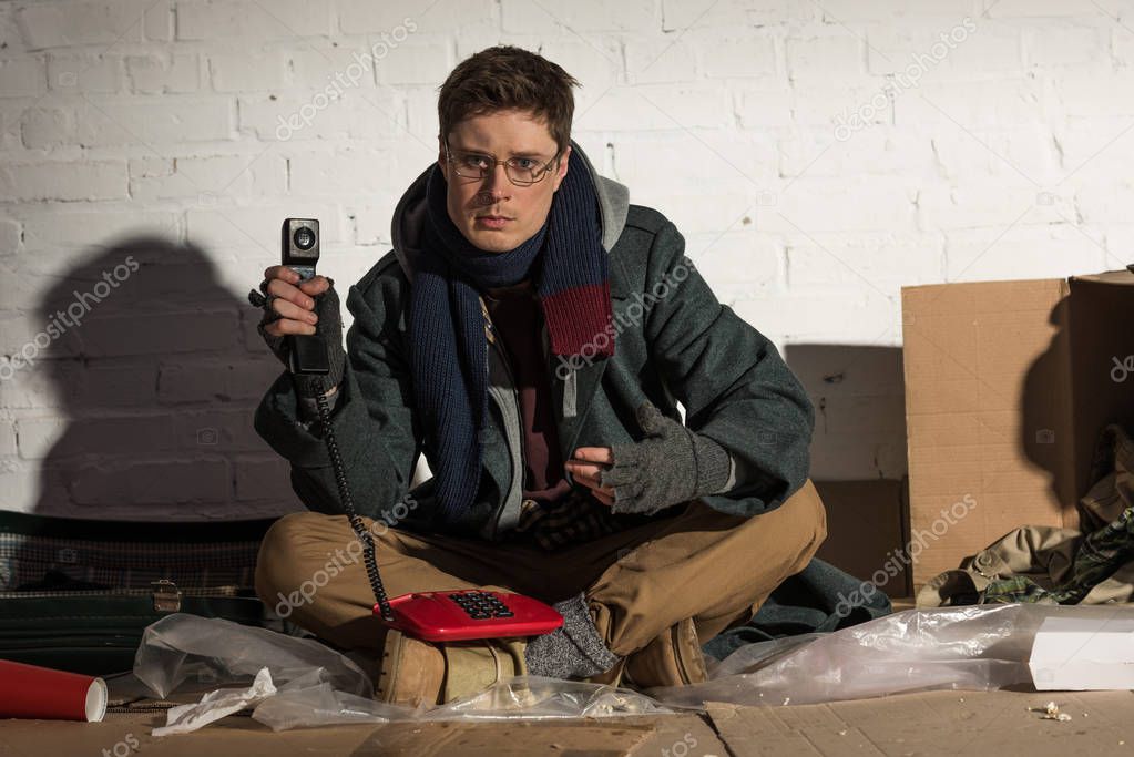 man in glasses holding red vintage telephone