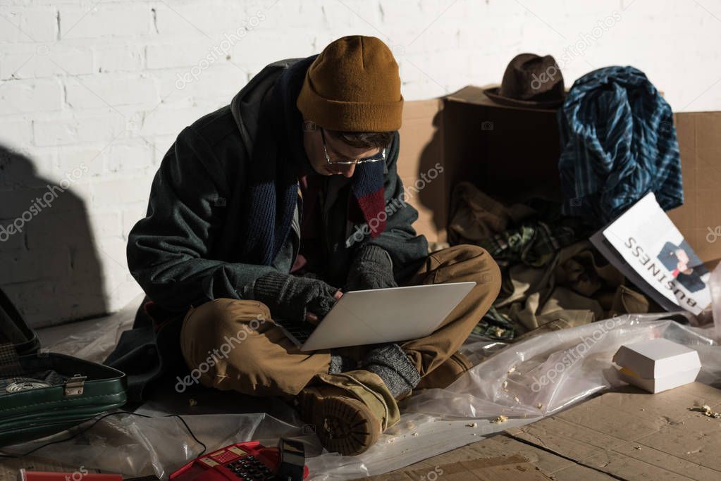 homeless man in glasses and fingerless gloves using laptop