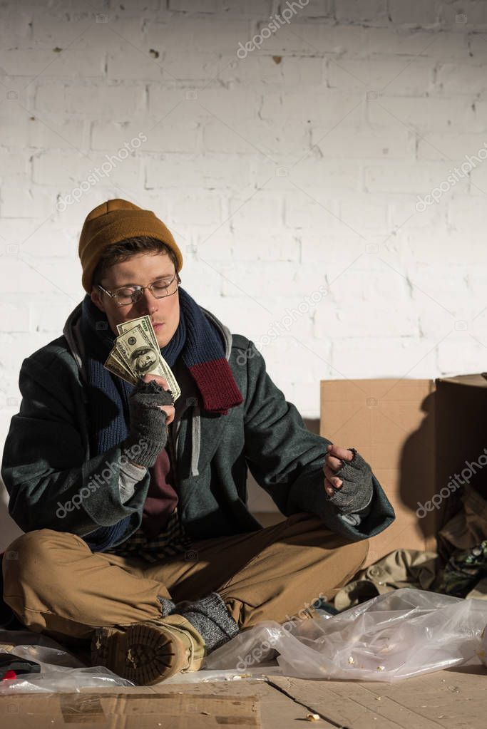 homeless man sitting on rubbish dump and holding money