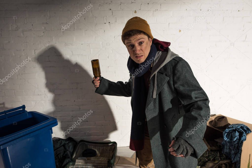 angry drunk homeless man holding empty bottle while standing in threatening pose