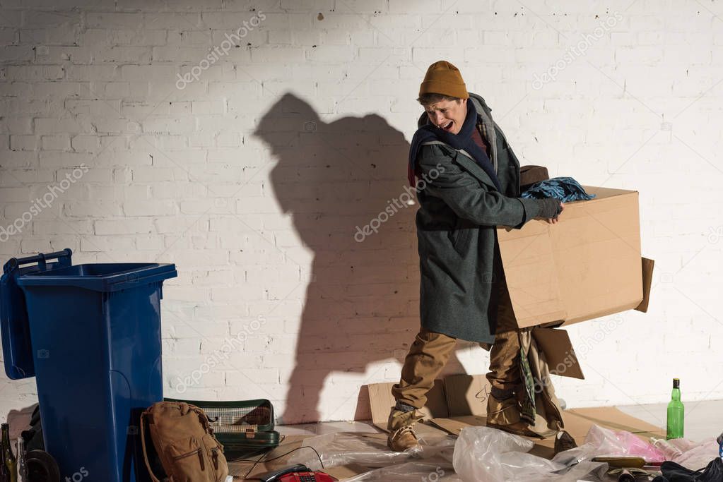 angry homeless man holding cardboard box with garbage