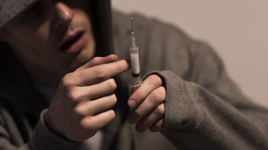 selective focus of junkie man holding syringe with dose of heroin clipart