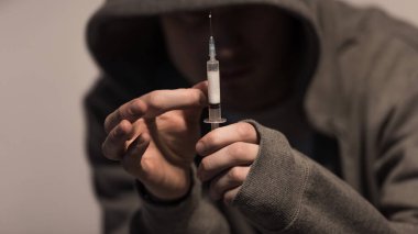selective focus of junkie man holding syringe with dose of heroin clipart