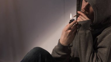addict man in hood lightening rolled marijuana cigarette clipart