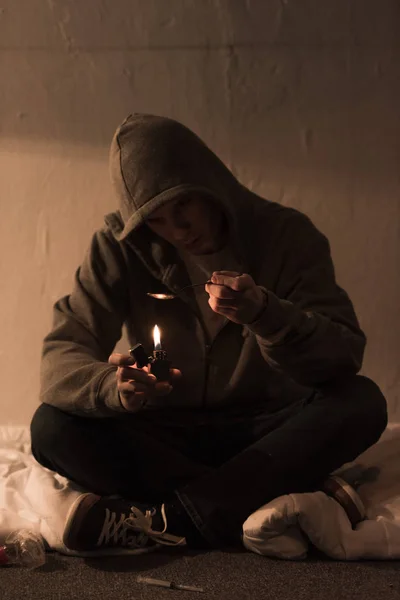 吸毒男子坐在黑暗的房间和加热勺子与海洛因打火机 — 图库照片