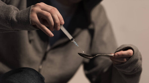 selective focus of addict man filling syringe with heroin