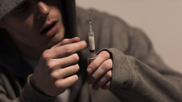 selective focus of junkie man holding syringe with dose of heroin