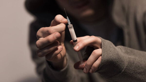 selective focus of addict man holding syringe with dose of heroin