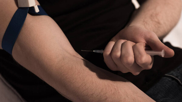 selective focus of junkie man making injection of heroin dose 