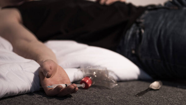 selective focus of lying man with syringe of heroin in hand