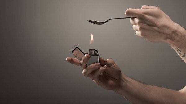 cropped view on junkie man heating spoon with heroin on lighter on grey background