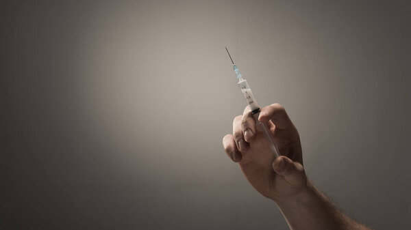 cropped view of male hand with heroin dose in syringe on grey background