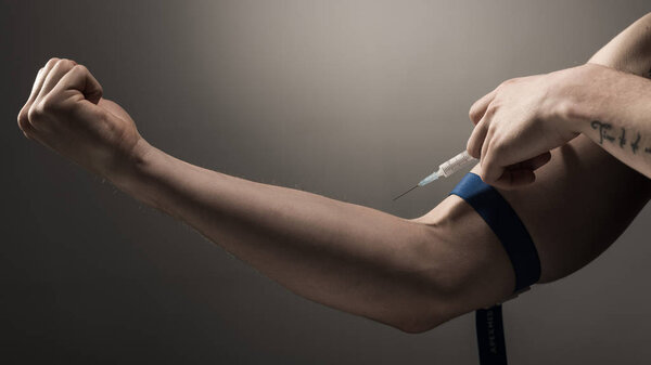 partial view of addict man making injection of heroin dose on grey background 