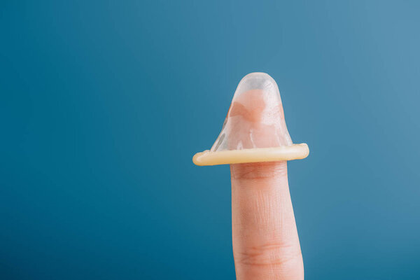 cropped view of male finger with condom isolated on blue, contraception concept