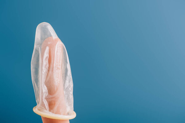 partial view of finger with condom isolated on blue, contraception concept