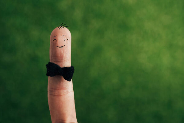 cropped view of cheerful male finger in bow tie on green