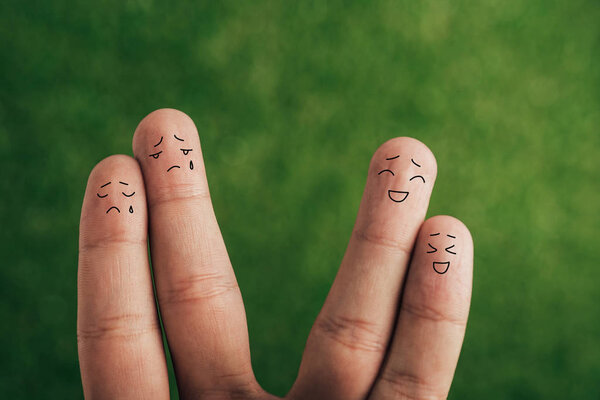 cropped view of crying and smiling couples of fingers on green