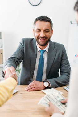 seçici odak masada oturan ve Doları banknot ofiste tutan yatırımcı wile kadın ile el sıkışan Danışmanı