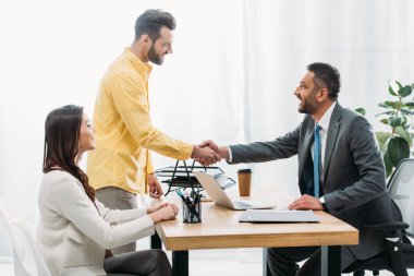 advisor and investor shaking hands over table wile woman sitting in office clipart