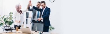 colleagues at table with laptop smiling and highing five in office clipart