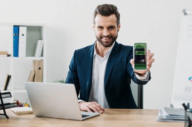 laptop ile masada oturan ve smartphone rezervasyon uygulaması ile Office ekranda gösterilen işadamı