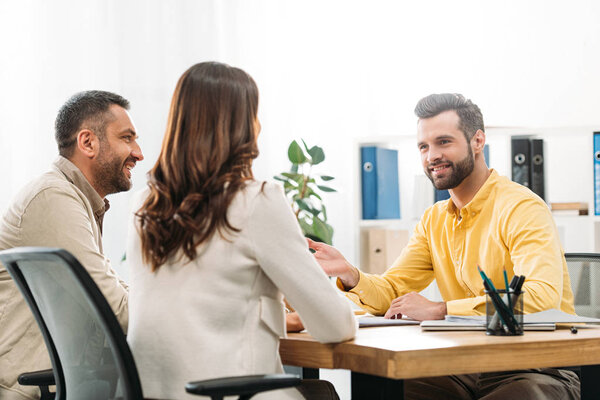 advisor sitting at table and smiling to man and woman in office