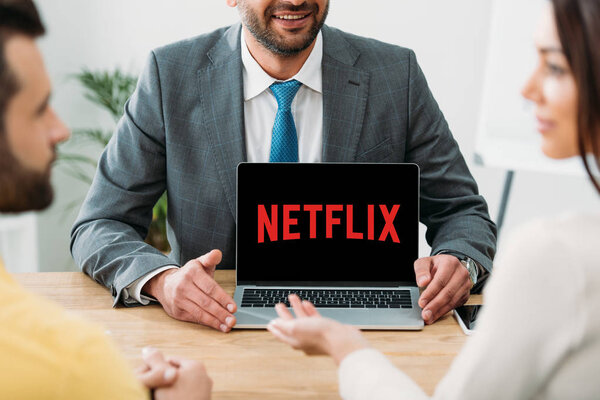 cropped view of advisor sitting at table and laptop with netflix website on screen with investors in office