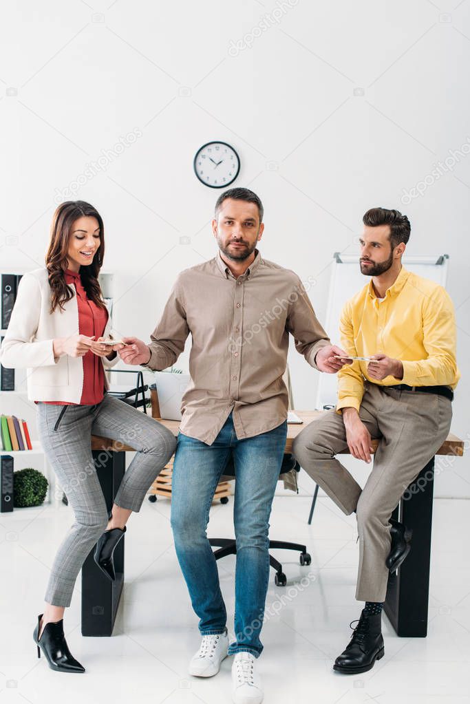 advisor standing and giving money to man and woman near table in office